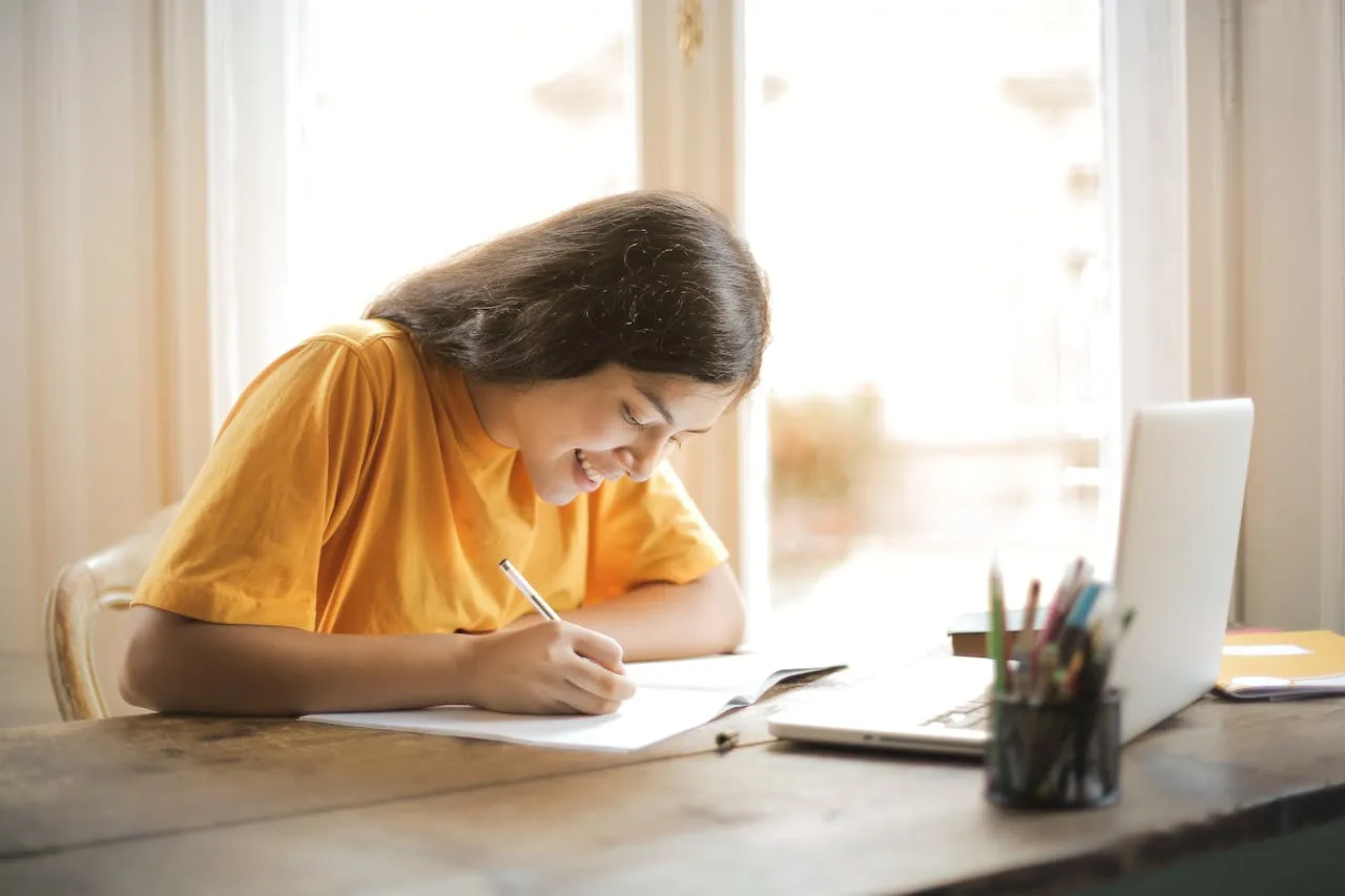Student writing notes at a desk while studying Chinese