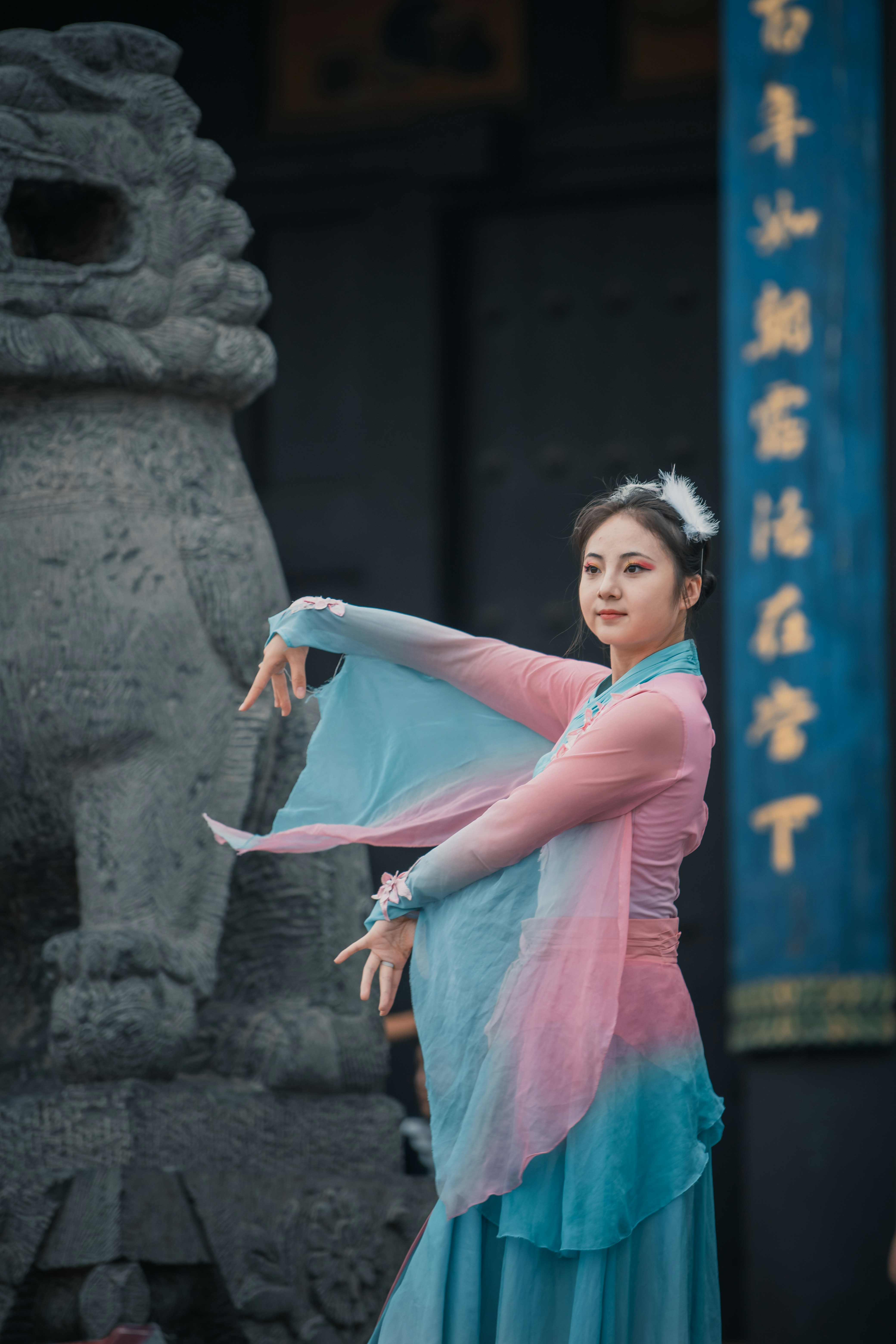 Chinese dancer in flowing traditional costume performing beside ancient stone guardian at temple
