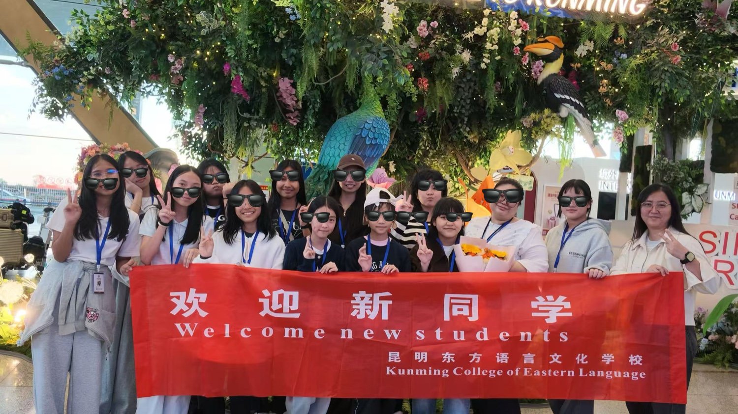KCEL staff welcoming an international student group at Kunming airport, holding a red Welcome New Students banner
